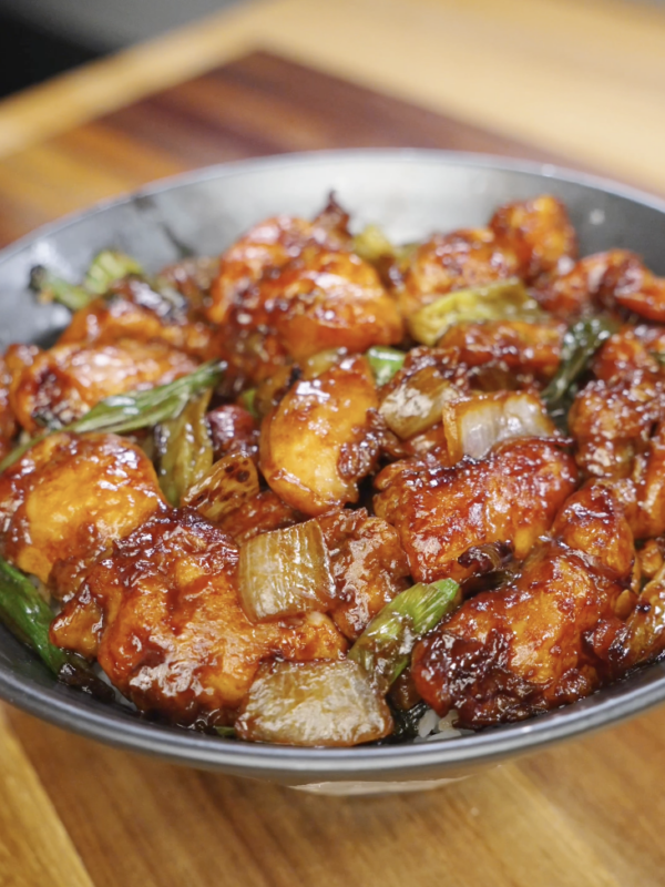 Finished Mongolian chicken tossed in a thick sweet and savory soy sauce with caramelized onions and scallions served over steamed rice.