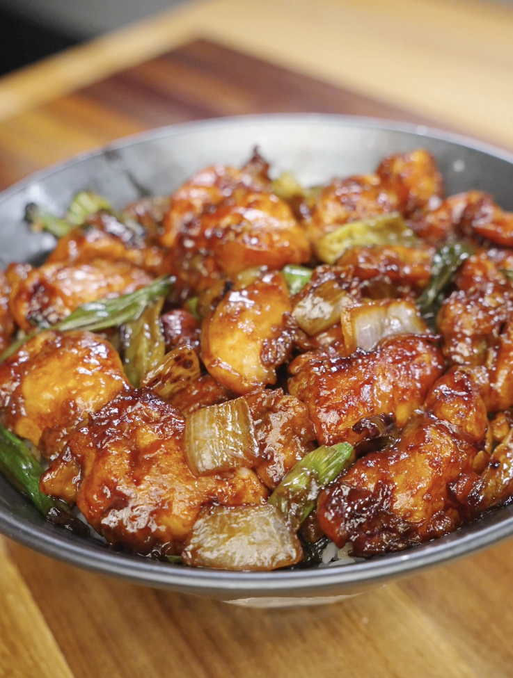 Finished Mongolian chicken tossed in a thick sweet and savory soy sauce with caramelized onions and scallions served over steamed rice.