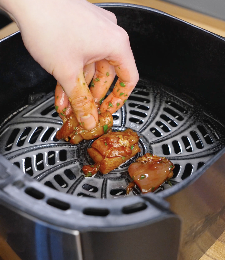 Hand placing cilantro honey marinated chicken thigh pieces into an air fryer basket in a single layer before cooking Sticky Cilantro Chicken at 375&deg;F.