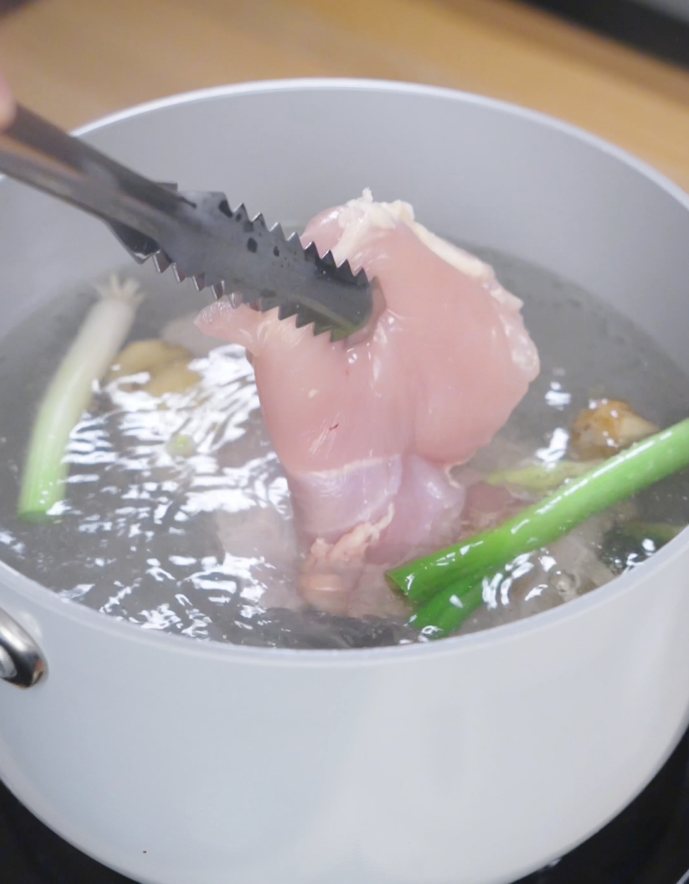 Boneless skinless chicken thighs gently poaching in simmering water with scallions, ginger, and garlic to create tender, flavorful ginger scallion chicken.