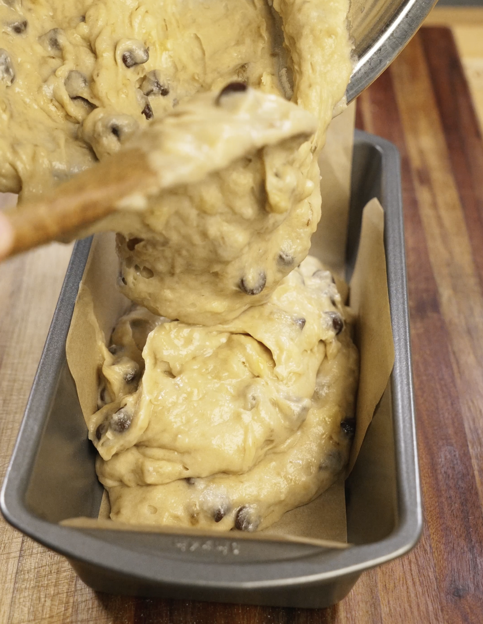 Chocolate chip banana bread batter being poured into a parchment-lined loaf pan, ready to be baked into a soft and moist homemade banana bread.