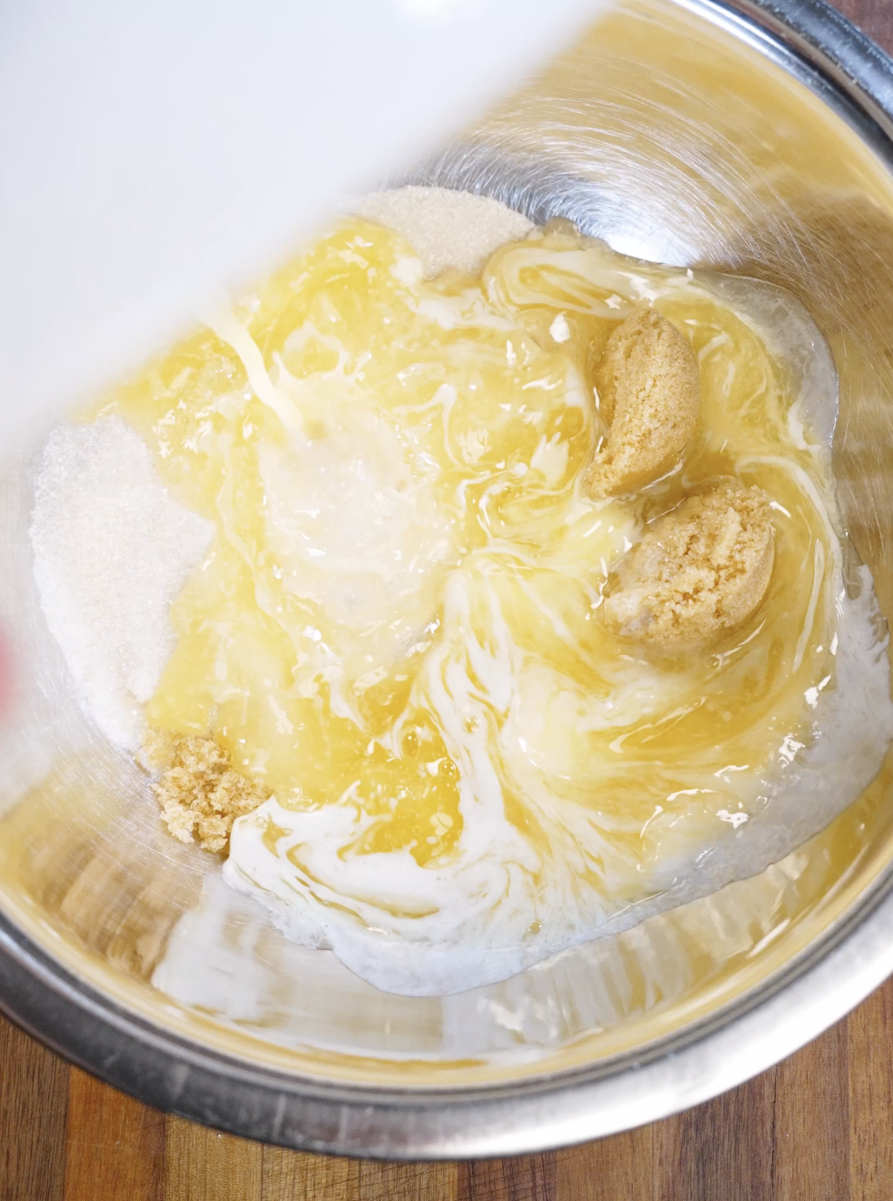 Melted butter being poured over granulated and brown sugar in a stainless steel bowl, the first step to creating shiny, crackly brownie cookie tops.