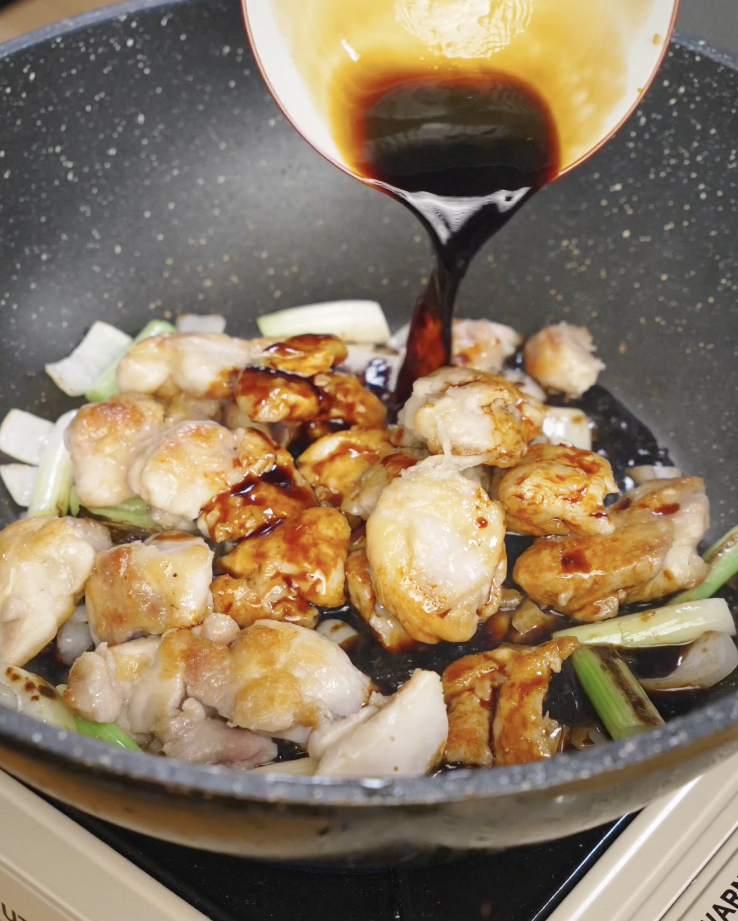 Dark sweet soy based Mongolian sauce being poured over seared chicken thighs and vegetables in a skillet to thicken and glaze.