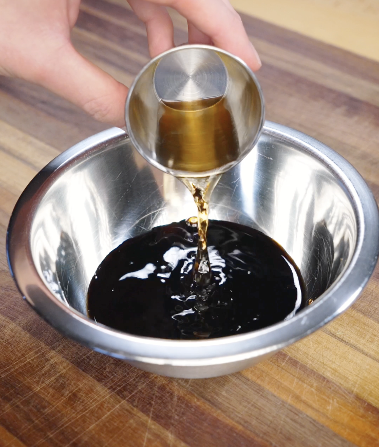 Shaoxing wine being poured from a metal measuring cup into a bowl of soy sauce and oyster sauce to make black pepper sauce for ground beef.