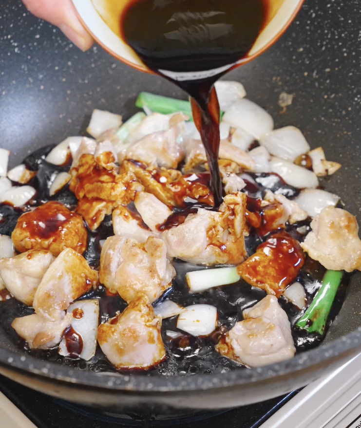Dark umami stir fry sauce being poured over seared chicken and onions in a skillet before thickening into a glossy glaze.