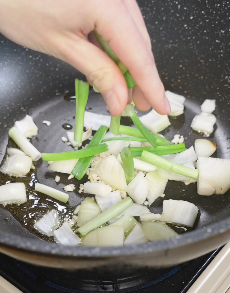 Minced garlic, thick onion wedges, and scallion whites saut&eacute;ing in oil in a nonstick skillet as the flavor base for black pepper ground beef.