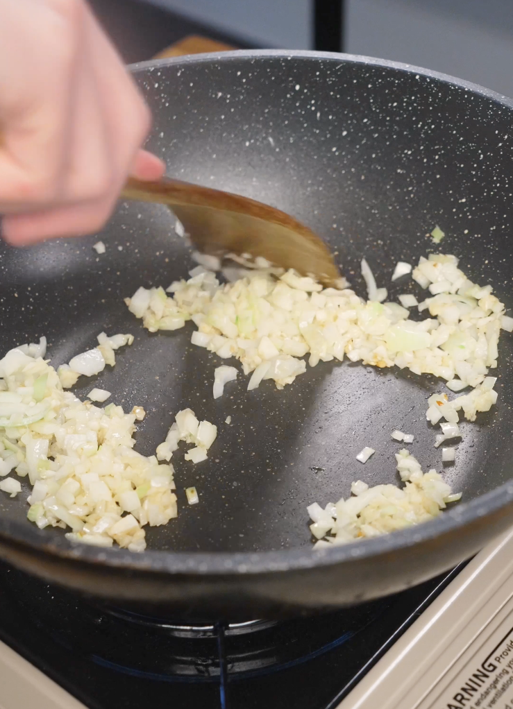 Finely diced onion being saut&eacute;ed in a nonstick pan until softened, forming the aromatic base for a quick Japanese ground beef curry.