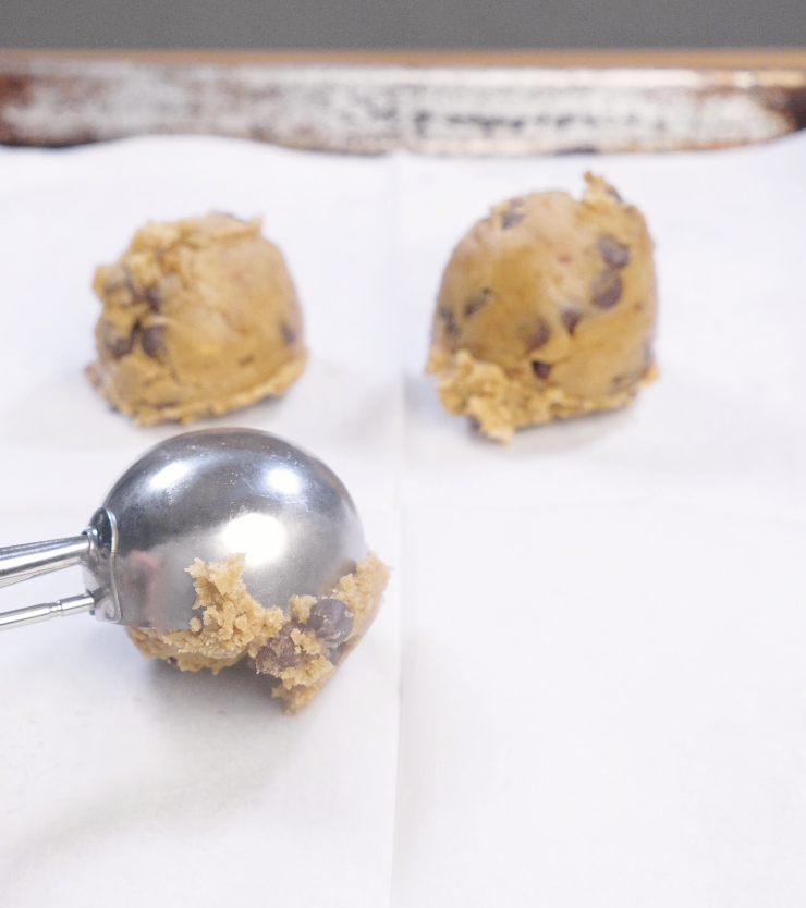Large scoops of brown butter chocolate chip cookie dough portioned onto parchment paper using a cookie scoop.