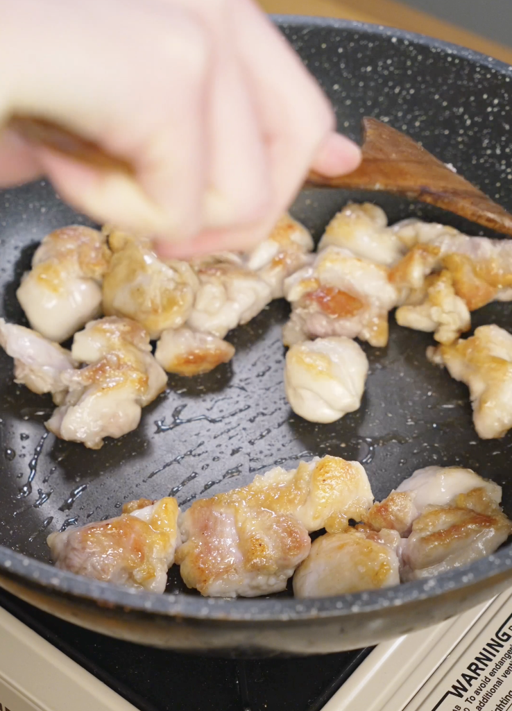 Marinated chicken thigh pieces searing in a hot skillet with oil, developing golden brown edges for Mongolian chicken.