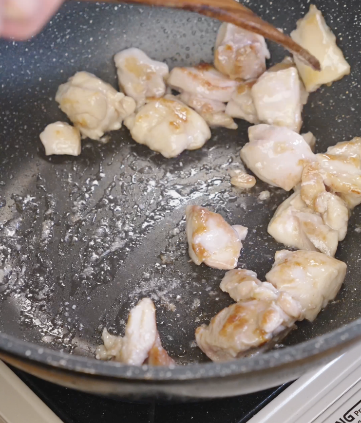 Marinated chicken thigh cubes cooking in a hot oiled pan, developing golden brown sear marks for Chicken Onion Stir Fry.