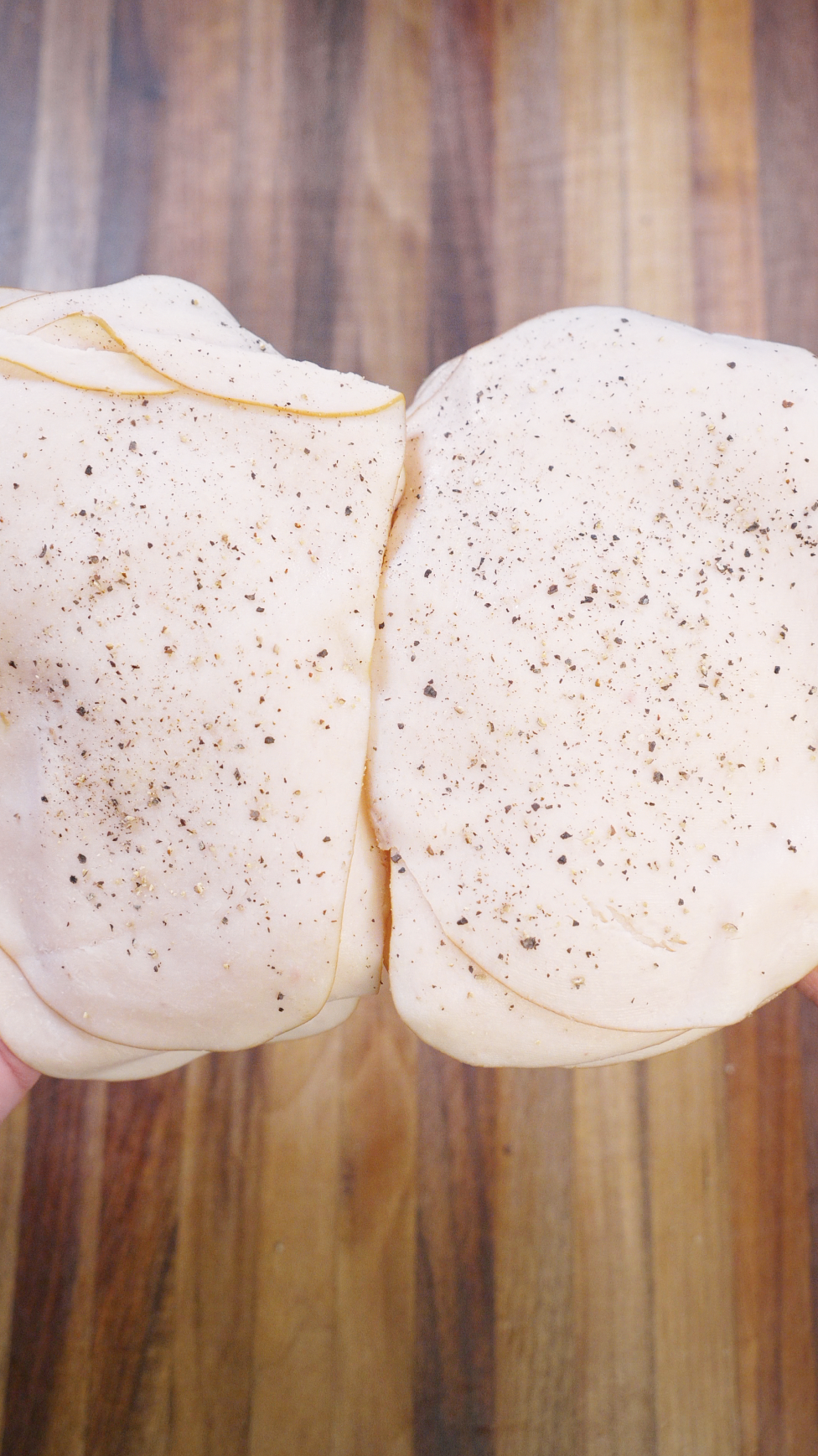 Two stacks of deli turkey seasoned with black pepper, ready to be seared and melted for a turkey pesto sandwich.