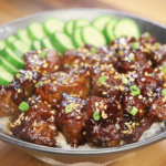 Finished soy garlic beef bowl made with tender caramelized beef cubes coated in a sticky soy garlic sauce, served over steamed white rice with sliced cucumbers, sesame seeds, and scallions as a healthy Asian dinner.