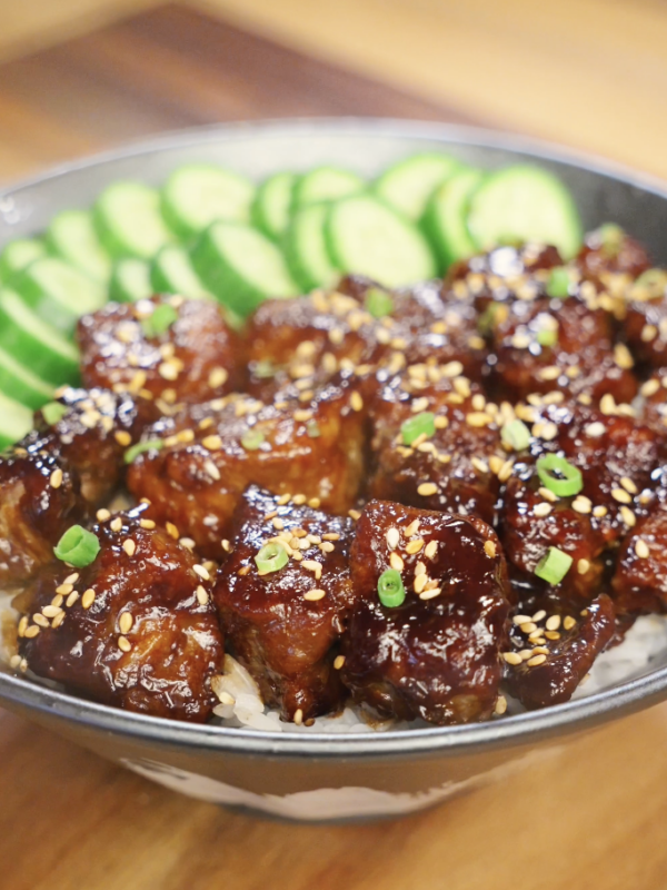 Finished soy garlic beef bowl made with tender caramelized beef cubes coated in a sticky soy garlic sauce, served over steamed white rice with sliced cucumbers, sesame seeds, and scallions as a healthy Asian dinner.