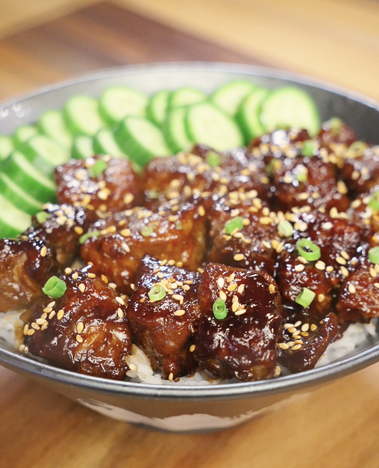 Finished soy garlic beef bowl made with tender caramelized beef cubes coated in a sticky soy garlic sauce, served over steamed white rice with sliced cucumbers, sesame seeds, and scallions as a healthy Asian dinner.