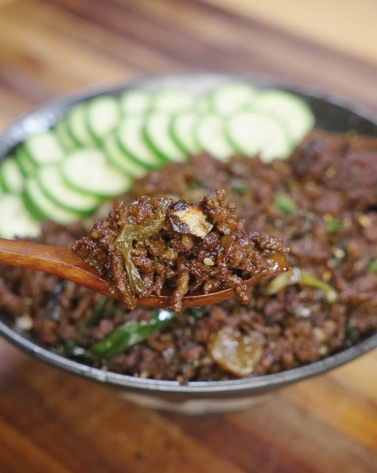 Wooden spoon lifting a bite of saucy black pepper ground beef with onions and scallions from a rice bowl, showing the glossy pepper sauce coating.