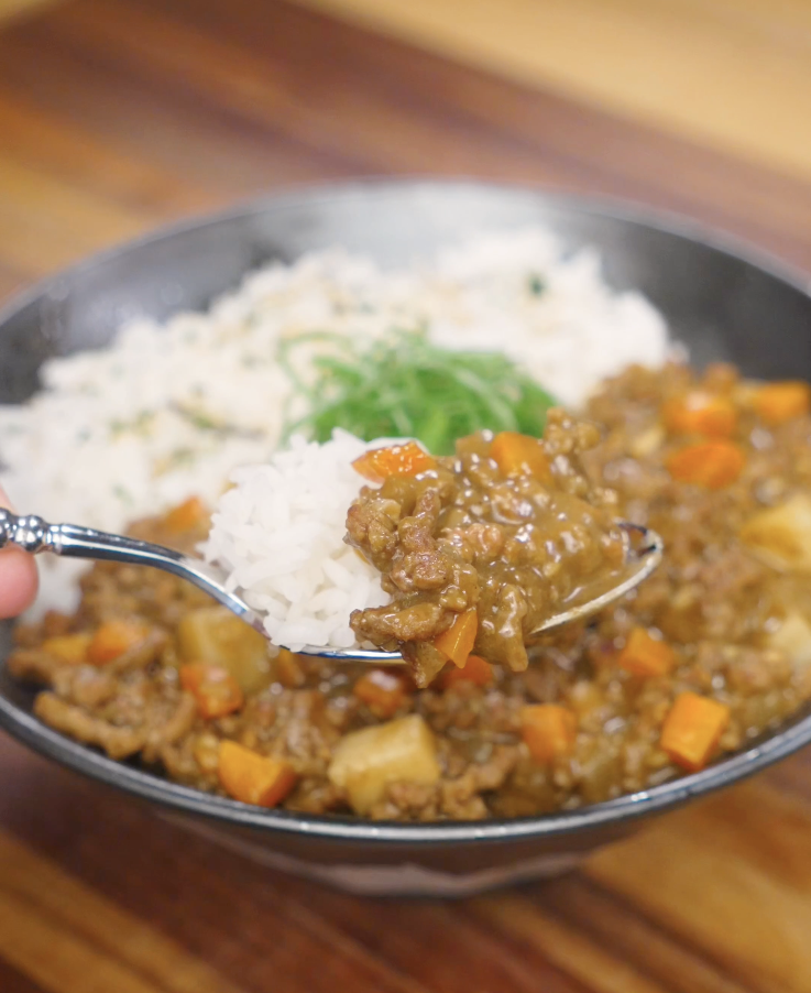 Spoon lifting a bite of Japanese ground beef curry with tender beef, carrots, potatoes, and rice, showcasing the thick and glossy curry sauce.