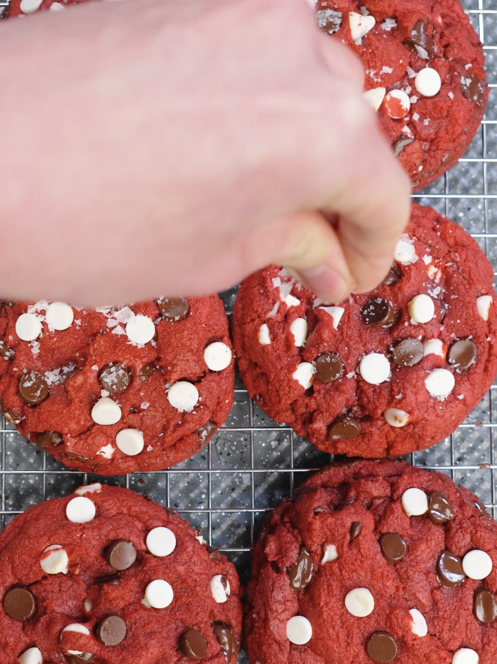 Hand sprinkling flaky sea salt over warm red velvet cookies to enhance sweetness and deepen the cocoa flavor.