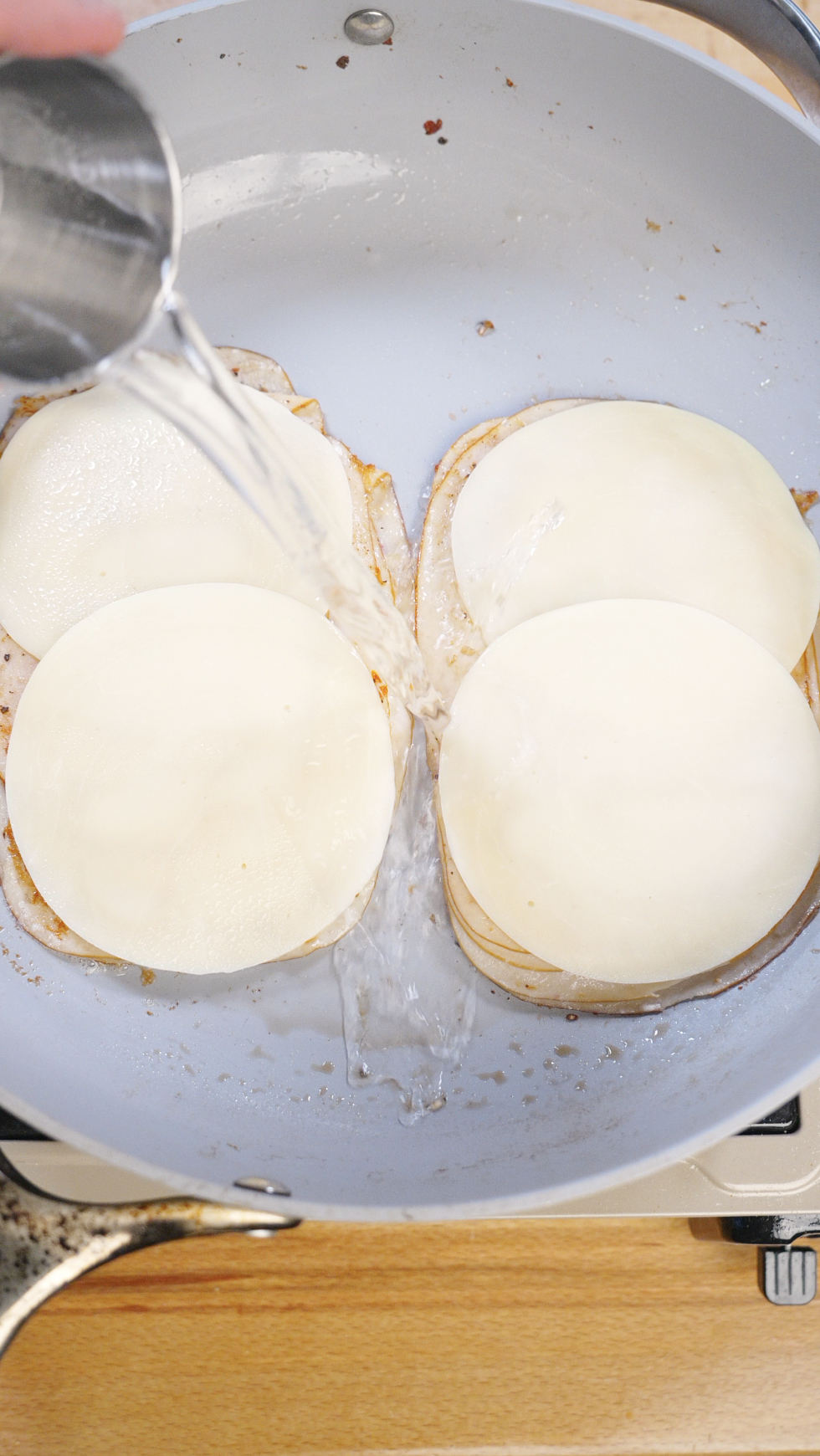 Water poured into a skillet to create steam and melt provolone cheese over seared turkey slices, ensuring a creamy and cohesive turkey pesto sandwich filling.