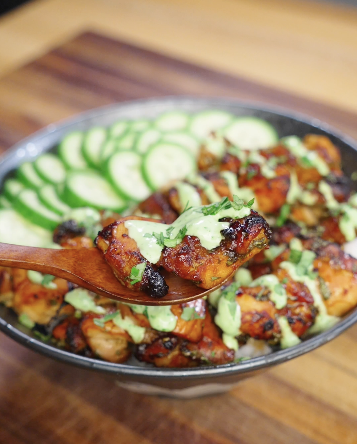 Close up of Sticky Cilantro Chicken on a wooden spoon, coated in glossy honey soy glaze and topped with creamy cilantro sauce, highlighting the caramelized exterior and juicy interior.