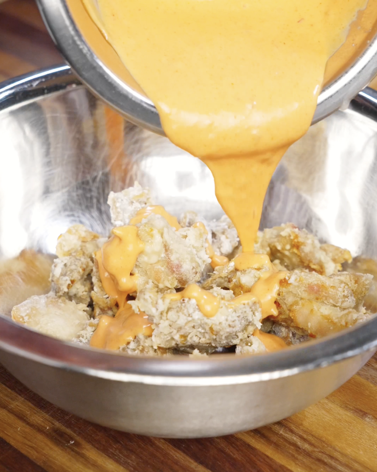 Crispy air fried chicken being coated evenly in thick homemade bang bang sauce for a sweet and spicy finish.