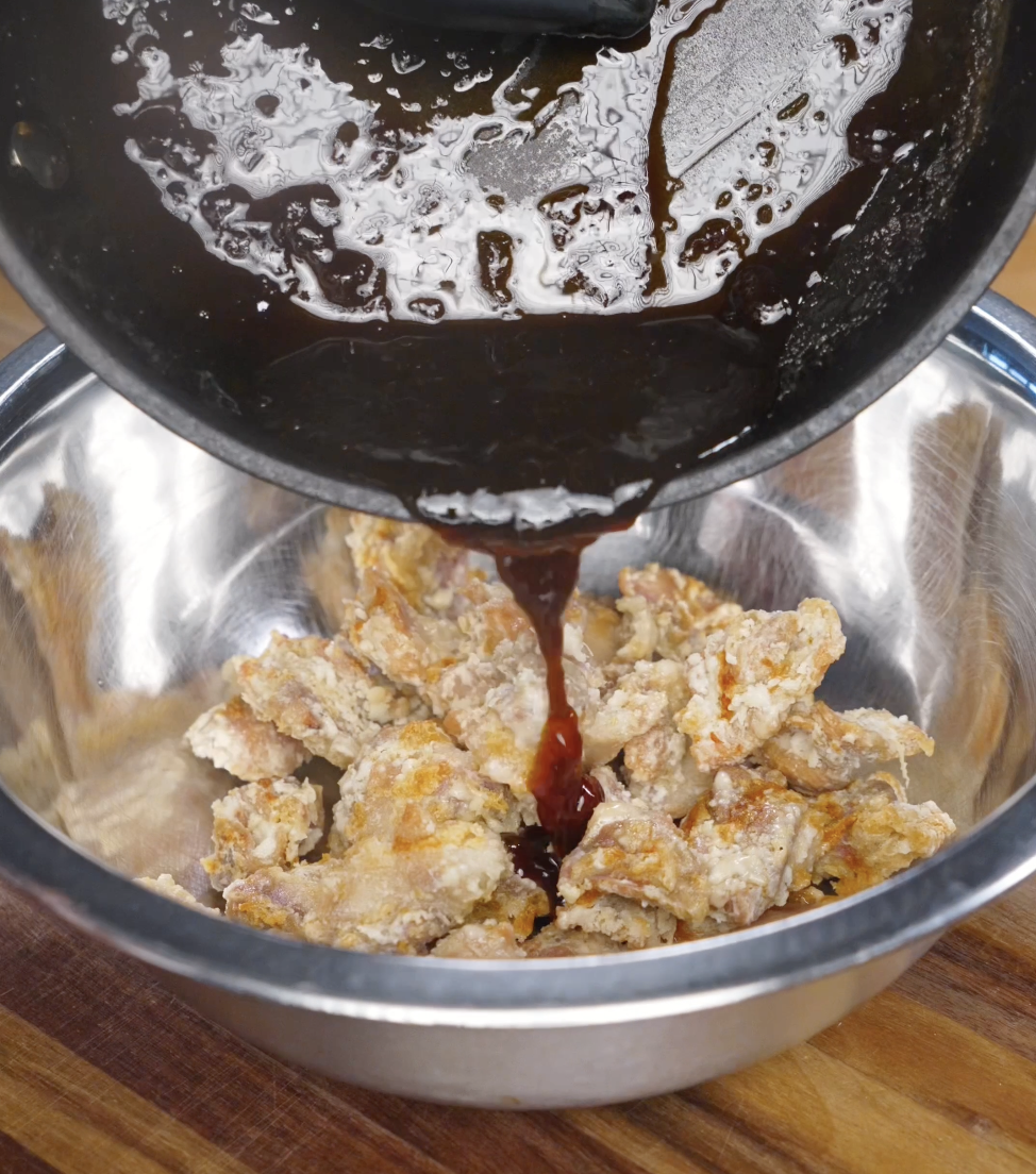 Hot soy garlic sauce being poured over air-fried crispy chicken pieces in a mixing bowl, coating each piece evenly with a sticky glaze.