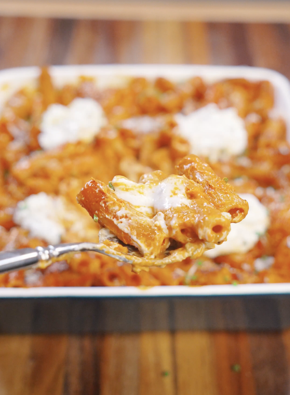 A fork lifting a creamy bite of rigatoni vodka pasta with tomato cream sauce and ricotta, showing the glossy sauce clinging to the noodles.