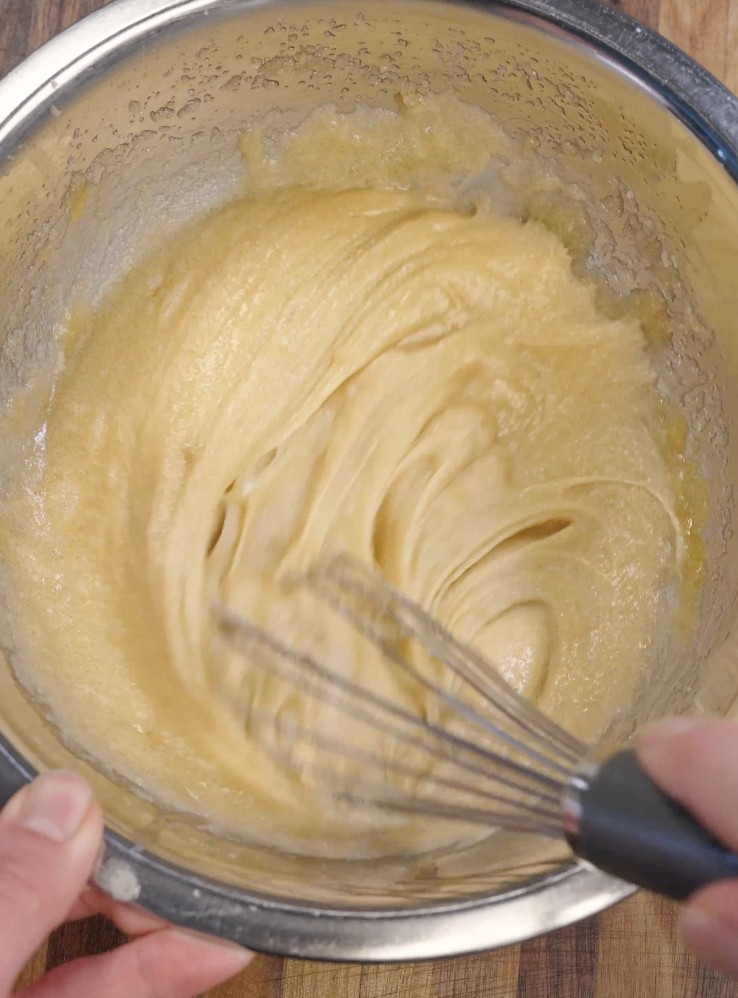 Brownie batter being vigorously whisked until thick, glossy, and smooth, a key step for achieving a shiny crackly top on fudgy Oreo brownies.