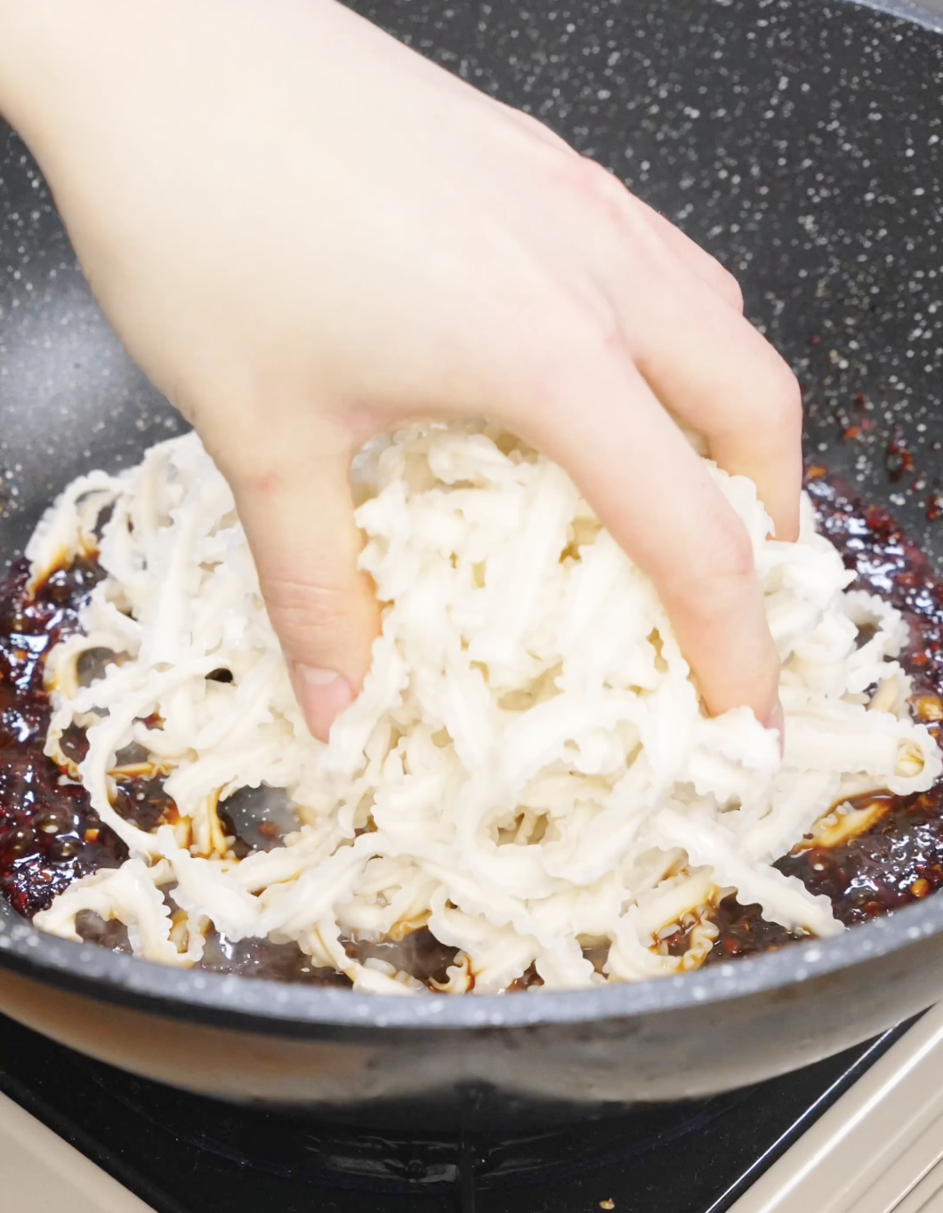 Cooked noodles being added into a pan of spicy chili garlic sauce.