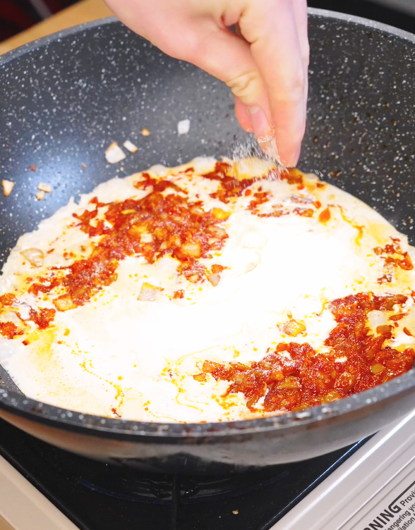 Heavy cream being poured into a pan with gochujang and aromatics while seasoning is added to form the creamy sauce for Creamy Sausage Pasta.