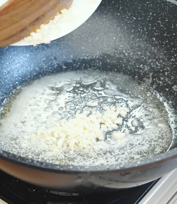 Minced garlic being added to melted butter in a pan to infuse the base of chili oil garlic butter noodle sauce.
