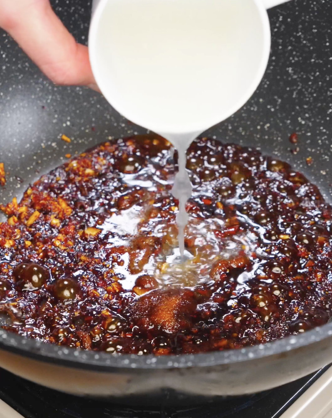 Starchy noodle water being poured into a pan of chili garlic sauce to help emulsify the sauce.