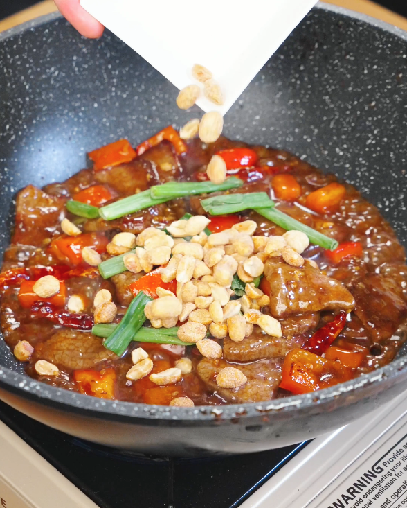 Roasted peanuts and scallions being added to the pan with Kung Pao Beef just before finishing the stir fry.