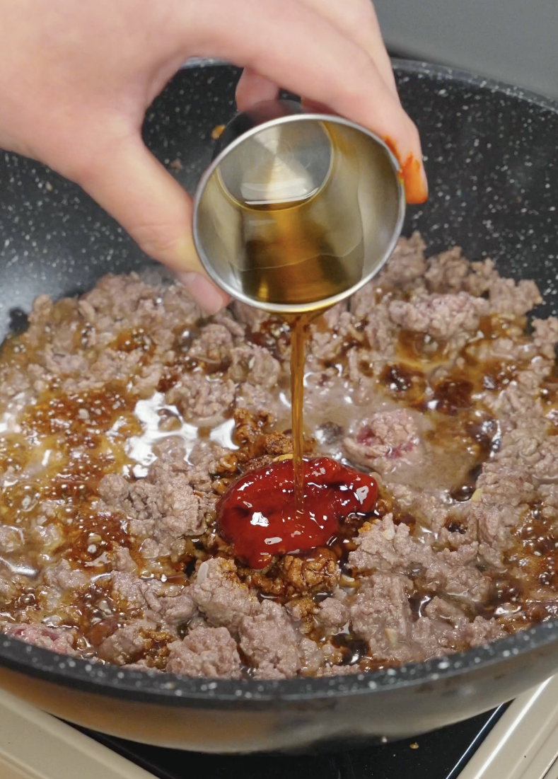 Gochujang soy sauce and sesame oil being added to ground beef in a pan for Korean ground beef recipe.