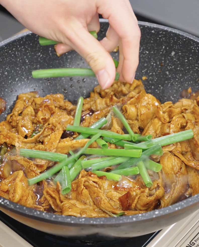 Fresh scallion greens being added into a pan of cooked pork belly to finish the garlic pork stir fry recipe.