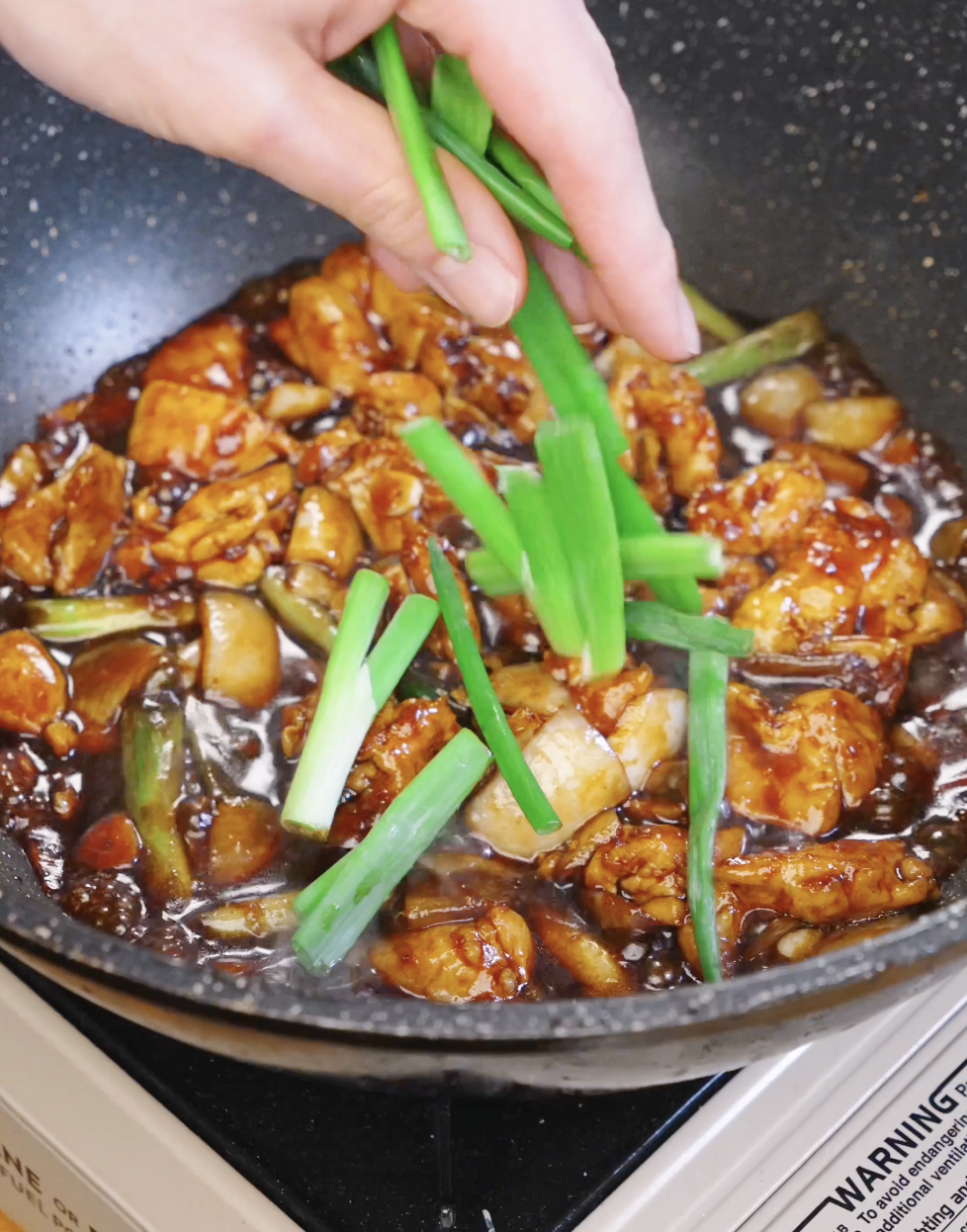 Fresh scallion greens being added to glossy honey garlic chicken as the sauce thickens in the pan.