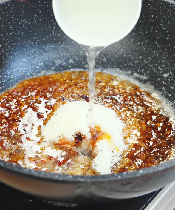 Water being poured into a pan with soy sauce, chili oil, sugar, parmesan, and garlic butter to create the chili oil garlic butter noodle sauce.