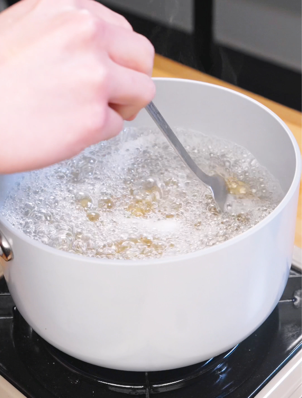 Rigatoni pasta boiling in a pot of salted water while being stirred with a fork as the first step in making Creamy Sausage Pasta.