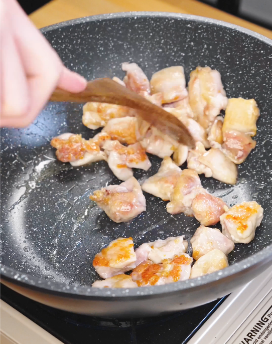 Cubed chicken thighs searing in a hot pan while being stirred with a wooden spatula to build flavor for honey cashew chicken.