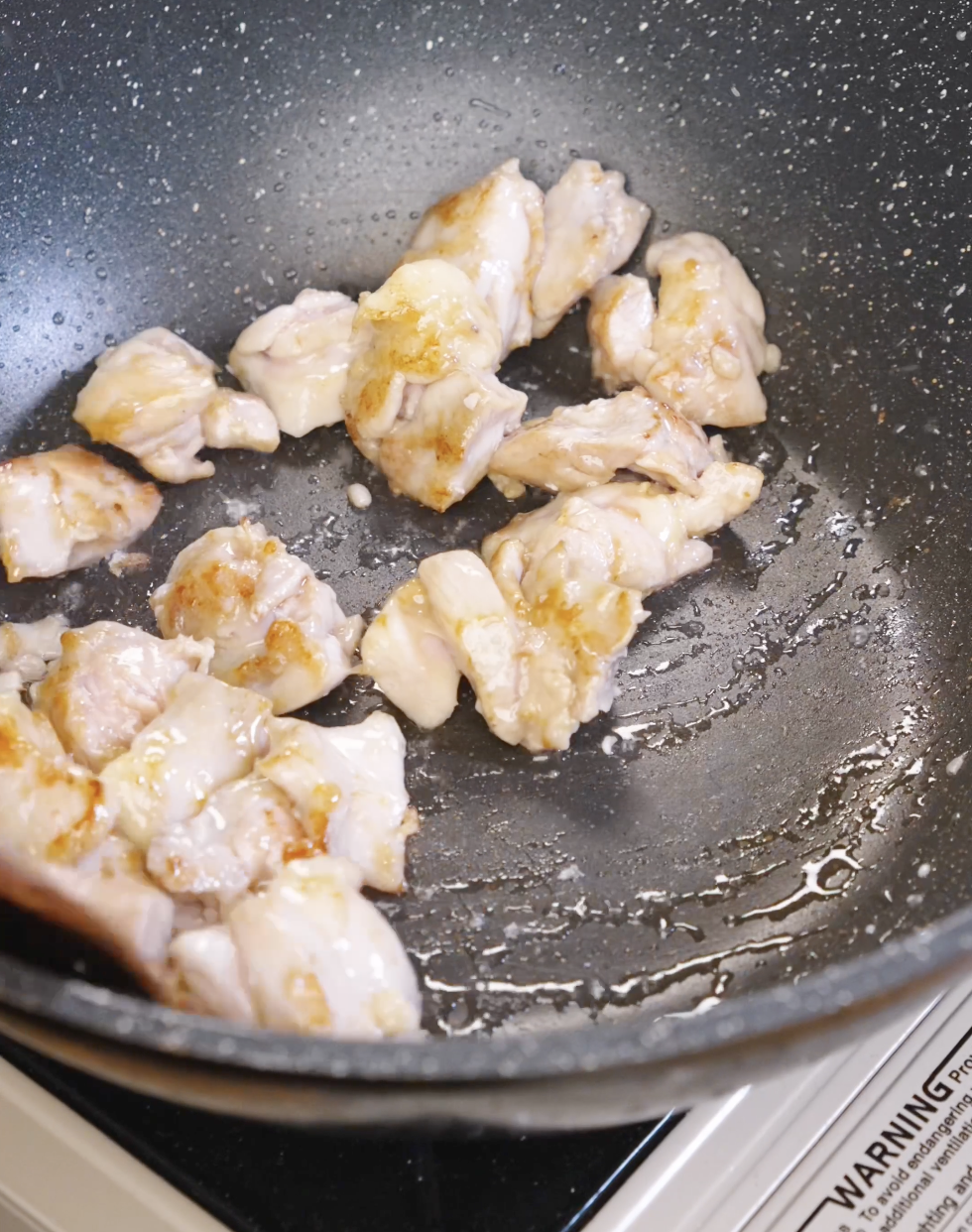 Marinated chicken thigh pieces searing in a hot pan to develop golden caramelized edges for honey garlic chicken stir fry.