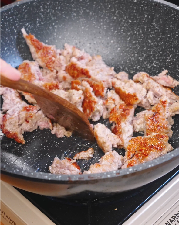Ground sausage cooking in a nonstick pan while being broken apart with a wooden spoon to develop flavor for Creamy Sausage Pasta.