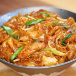 Bowl of chicken chow fun with glossy wide rice noodles, tender chicken slices, bean sprouts, onions, and scallions coated in savory soy sauce.