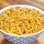 Bowl of chili oil garlic butter noodles coated in glossy buttery chili sauce and topped with sesame seeds, chili flakes, and sliced scallions.