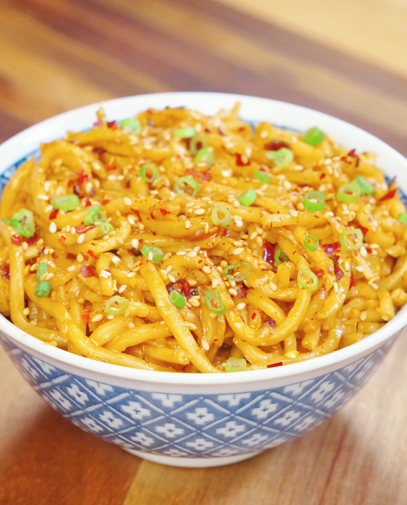 Bowl of chili oil garlic butter noodles coated in glossy buttery chili sauce and topped with sesame seeds, chili flakes, and sliced scallions.