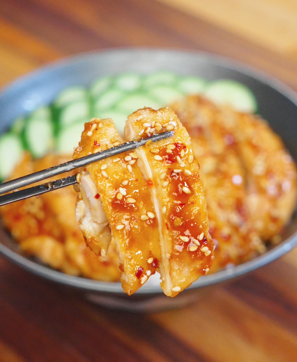 Chopsticks lifting a piece of Honey Chili Chicken coated in glossy honey chili glaze with sesame seeds.