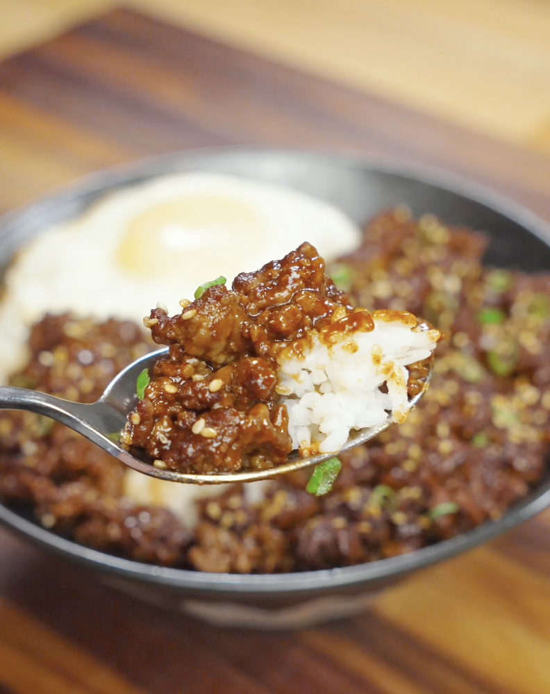 Spoon lifting a bite of Korean ground beef recipe with rice coated in glossy gochujang sauce.