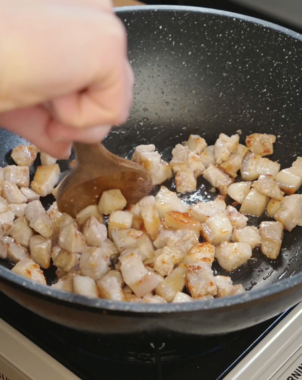 Small cubes of pork belly sizzling in a pan as they cook and render fat to create crispy golden edges for fried rice.