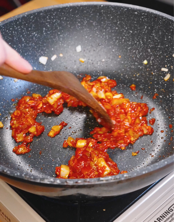 Gochujang paste being stirred with onions and garlic in a pan as the base of the sauce for Creamy Sausage Pasta.