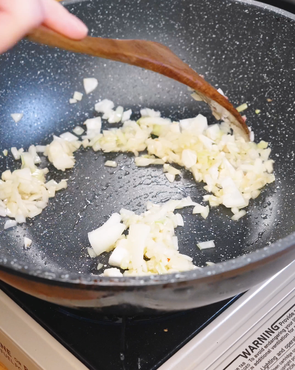Diced onion and minced garlic sautéing in a pan with rendered sausage fat to build flavor for Creamy Sausage Pasta sauce.