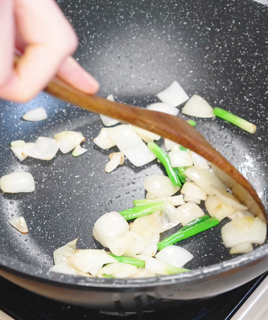 Onion wedges and scallion whites saut&eacute;ing in a hot pan to build the aromatic base for honey cashew chicken.