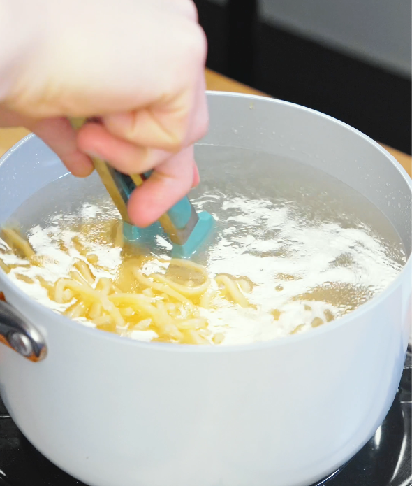 Instant ramen noodles being separated with tongs in a pot of boiling water while cooking for chili oil garlic butter noodles.